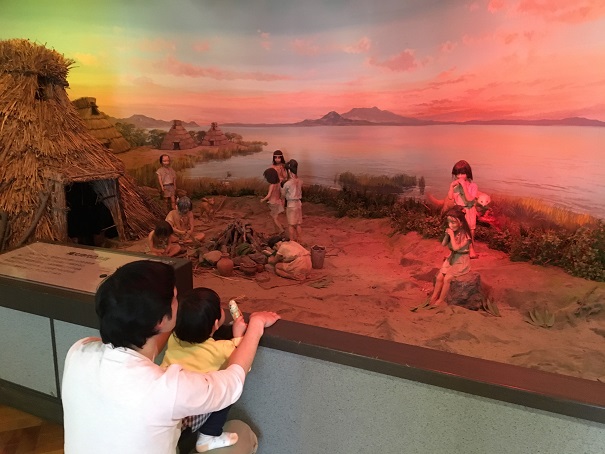 縄文時代の藁の家や生活している人々のジオラマと近くで見学している親子の写真