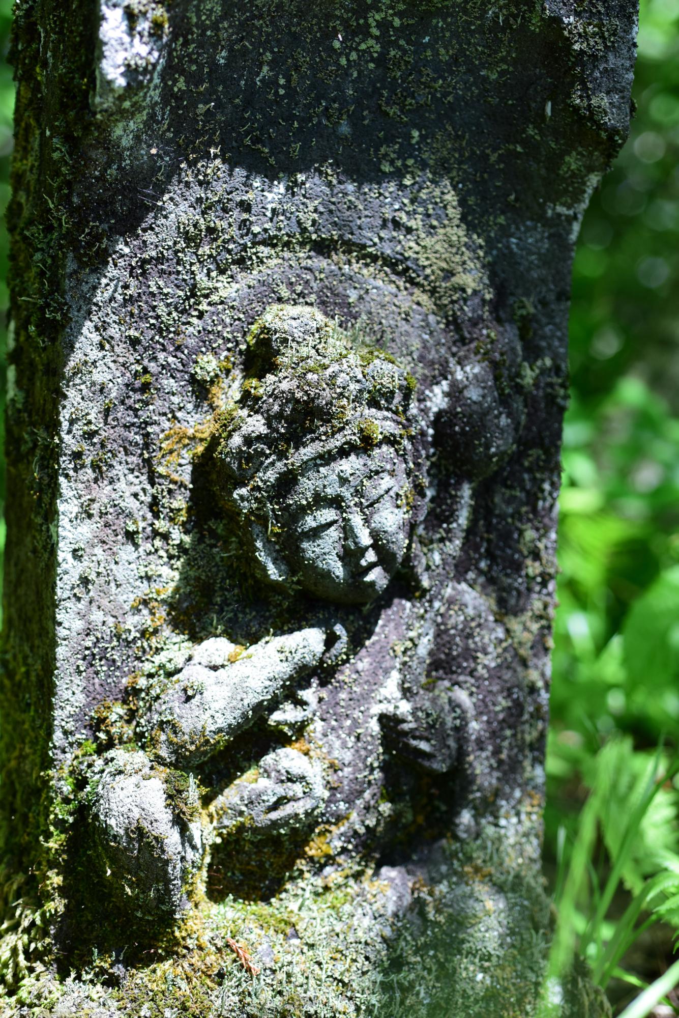 苔が生えた石に彫られている観音像の写真
