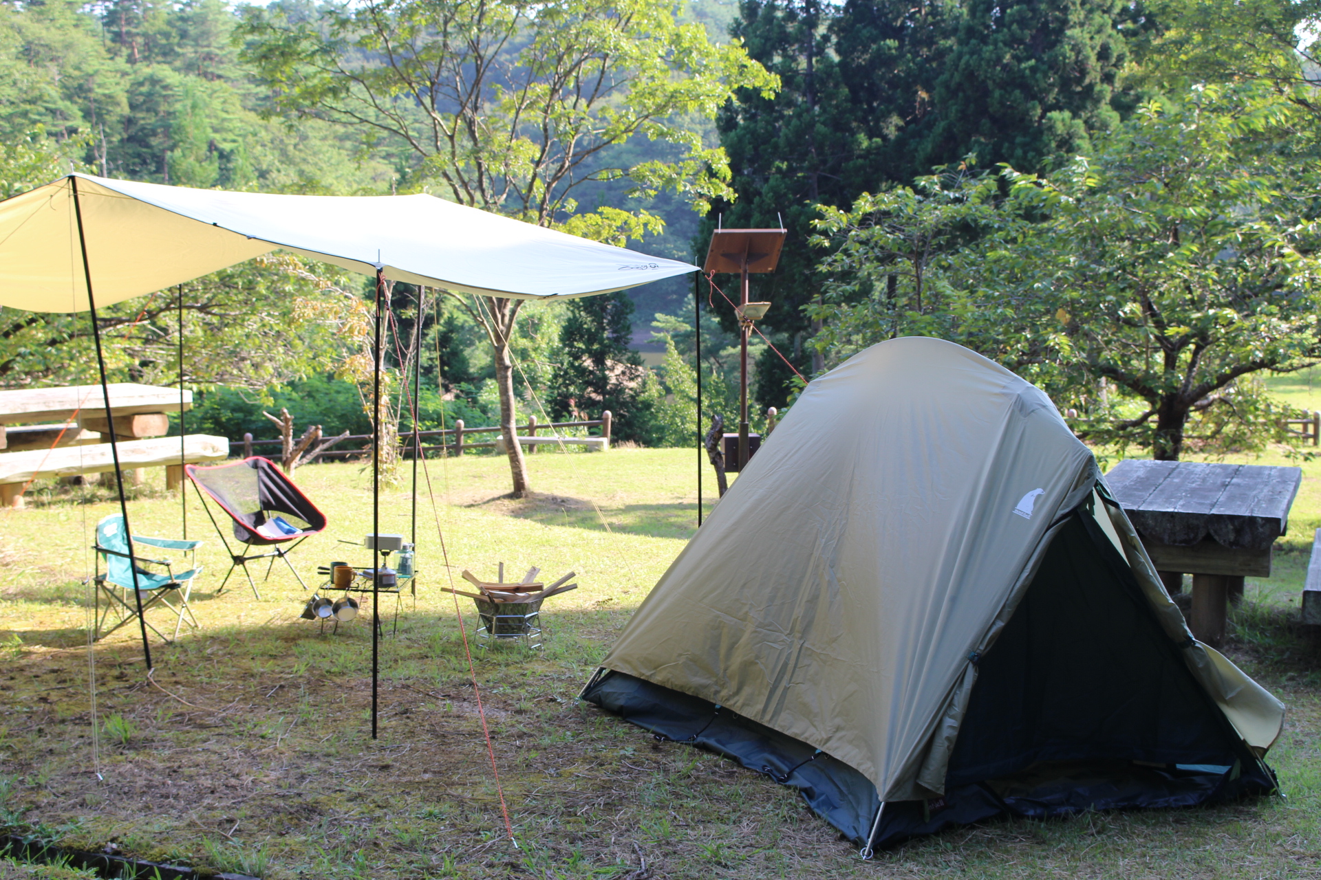 緑の木々に囲まれた芝生の上に、テントとタープテント、キャンピングチェアが置かれた、はねがわキャンプ場の写真