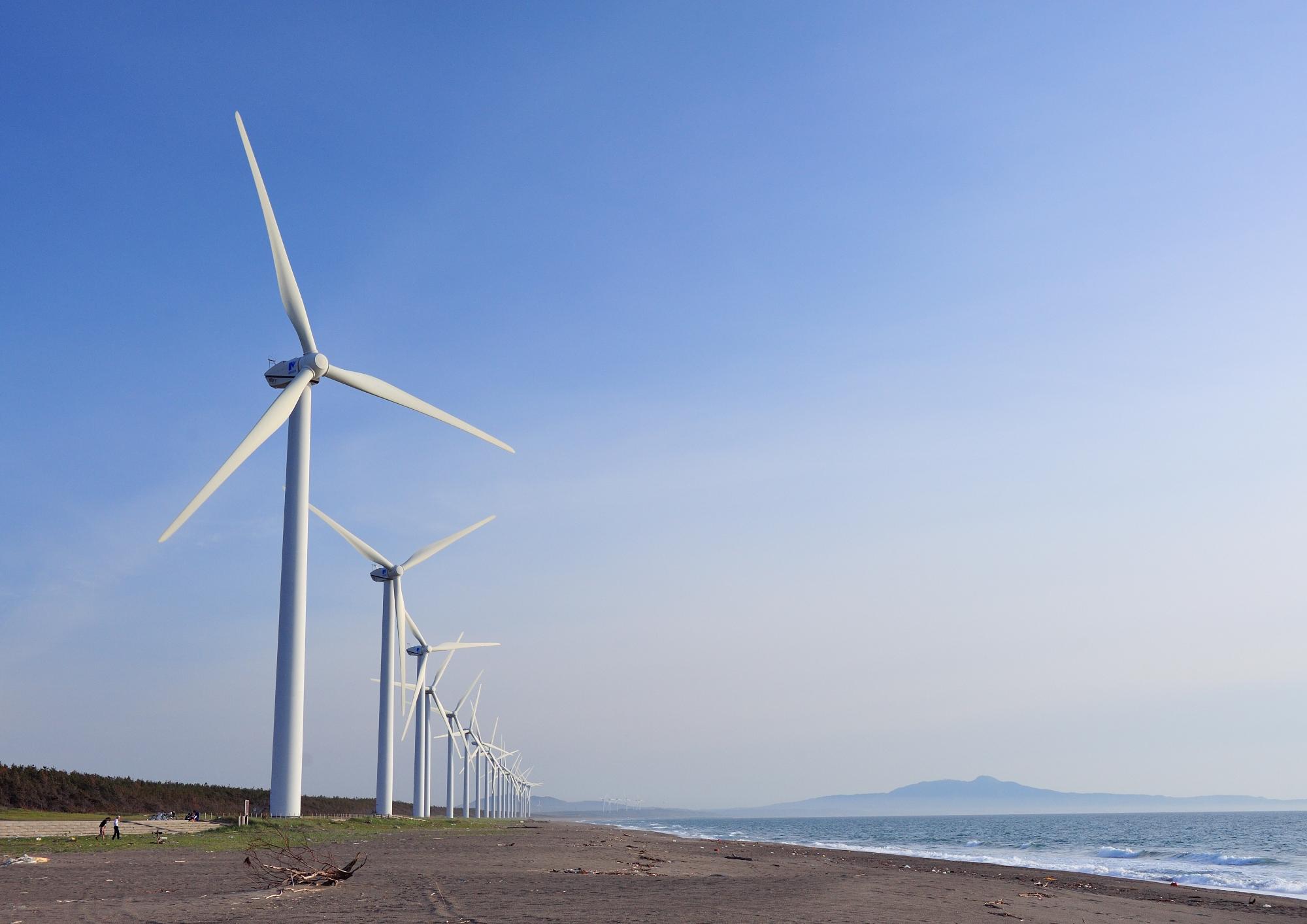 3枚の羽根がある大きな風力発電装置が海辺に並んでいる写真